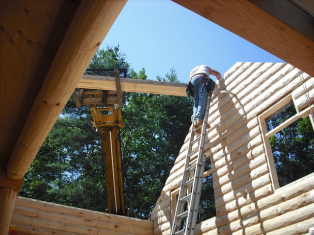 Man on ladder working on log home construction.